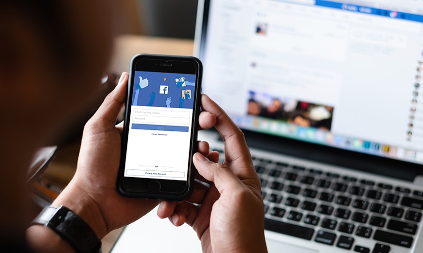 imagem de uma pessoa segurando um celular conectado na página do Facebook, representando o assunto do artigo da agência de marketing digital